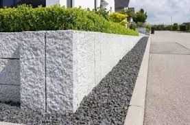 a stone planter on the side of a road in front of a house with bushes