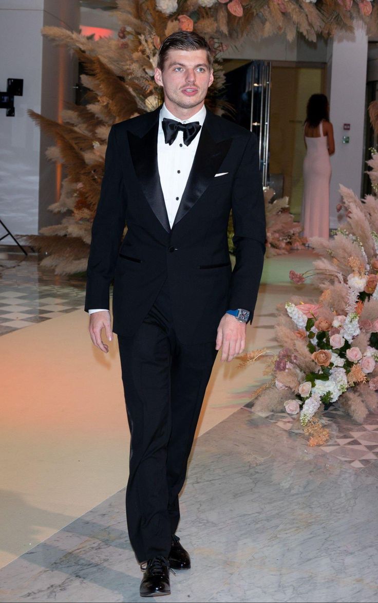 a man in a tuxedo is walking down the aisle with flowers on either side