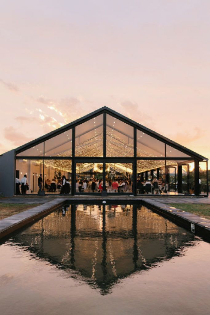 a group of people standing outside of a building next to a lake at sunset or dawn