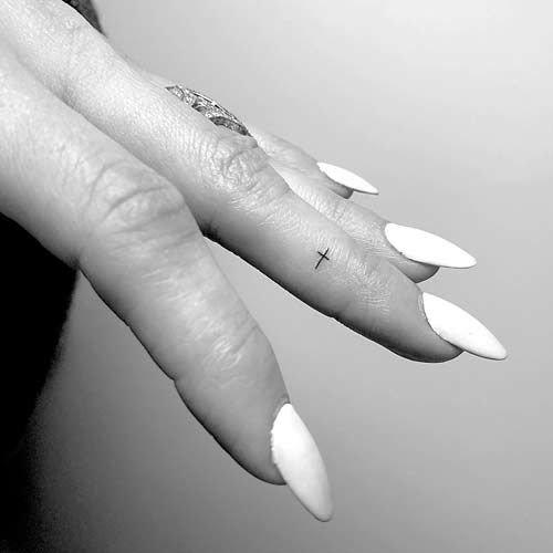 a woman's hand with white manies and a cross tattoo on her finger