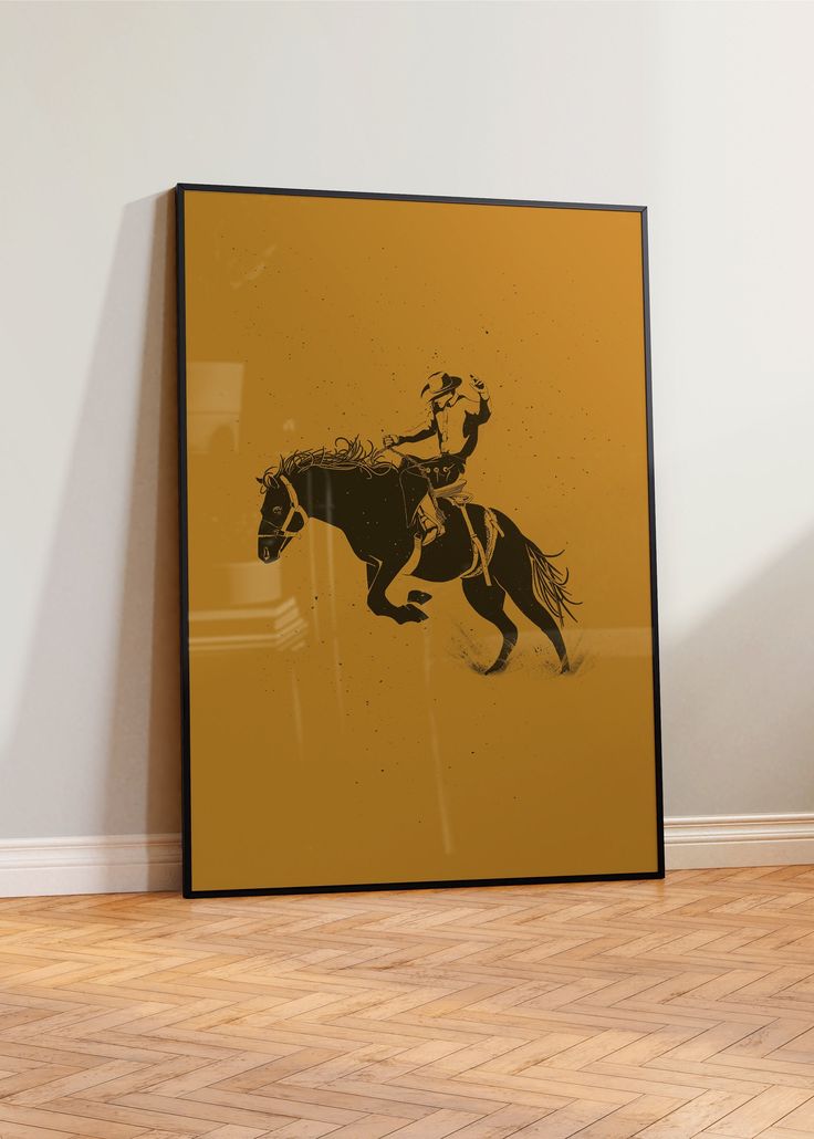 a framed photograph of a man riding a horse on a wooden floor in front of a white wall