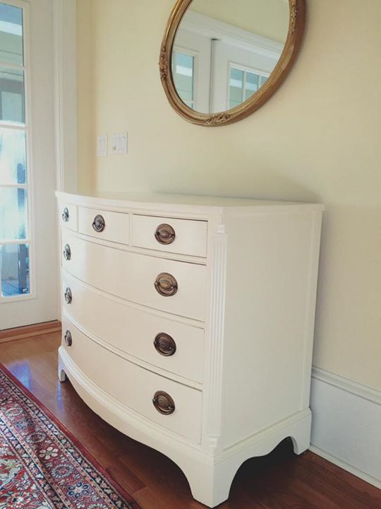 a white dresser sitting on top of a hard wood floor next to a wall mounted mirror