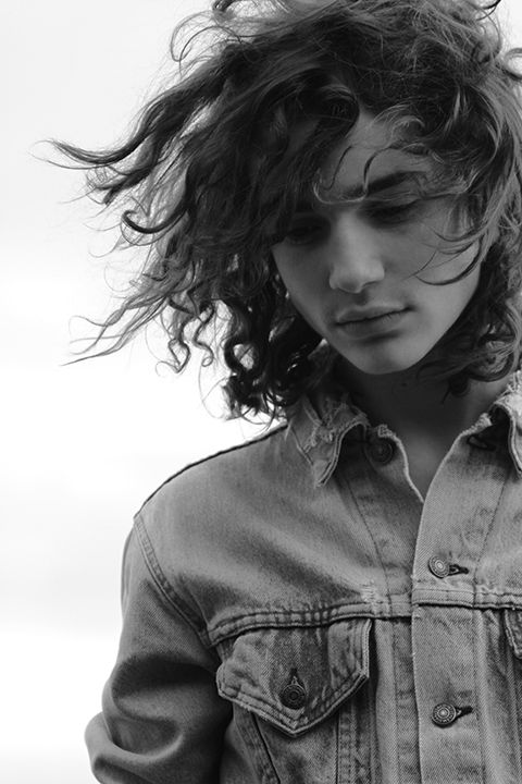 a woman with curly hair is looking down at her cell phone while wearing a denim shirt