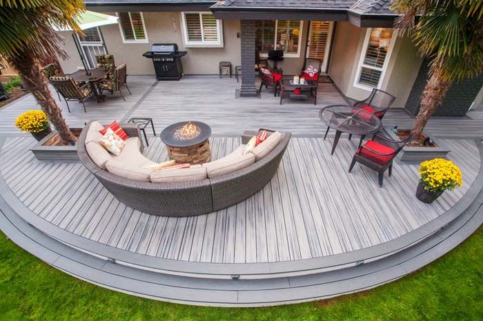 an outdoor deck with seating and fire pit surrounded by palm trees in front of a house