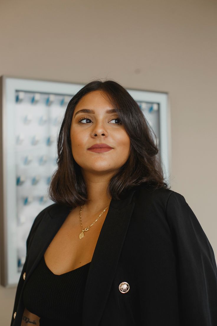 a woman standing in front of a mirror wearing a black blazer and gold necklace