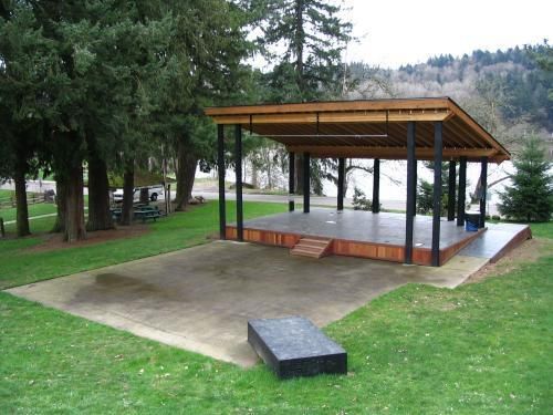 a covered area in the middle of a park with benches on it and trees around