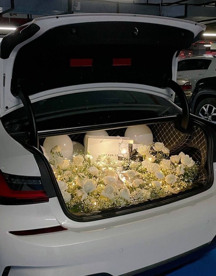 the trunk of a white car with candles in it and flowers on the floor inside