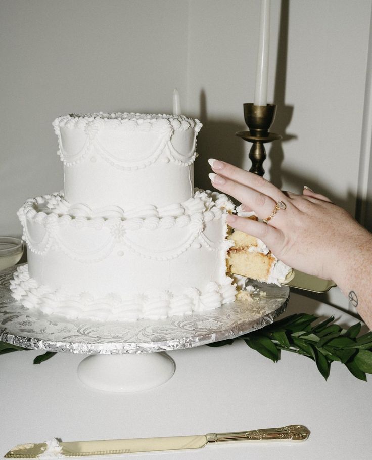 a person cutting into a white wedding cake on top of a table next to a knife and fork