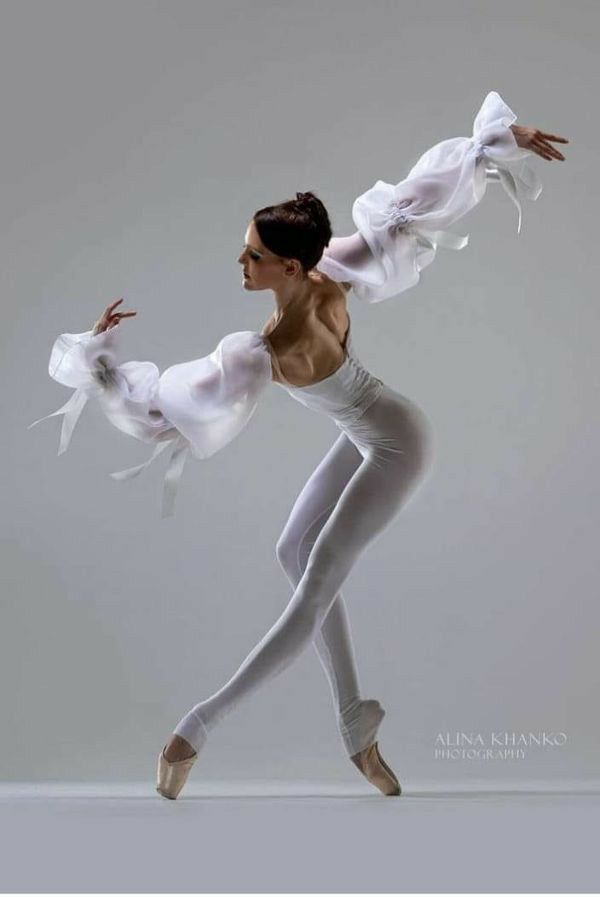 a woman in white is dancing with her arms spread out to the side and one leg bent