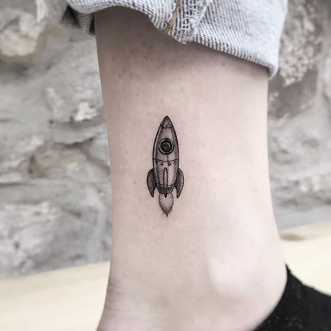 a small tattoo on the ankle of a woman with a rocket ship in it's center