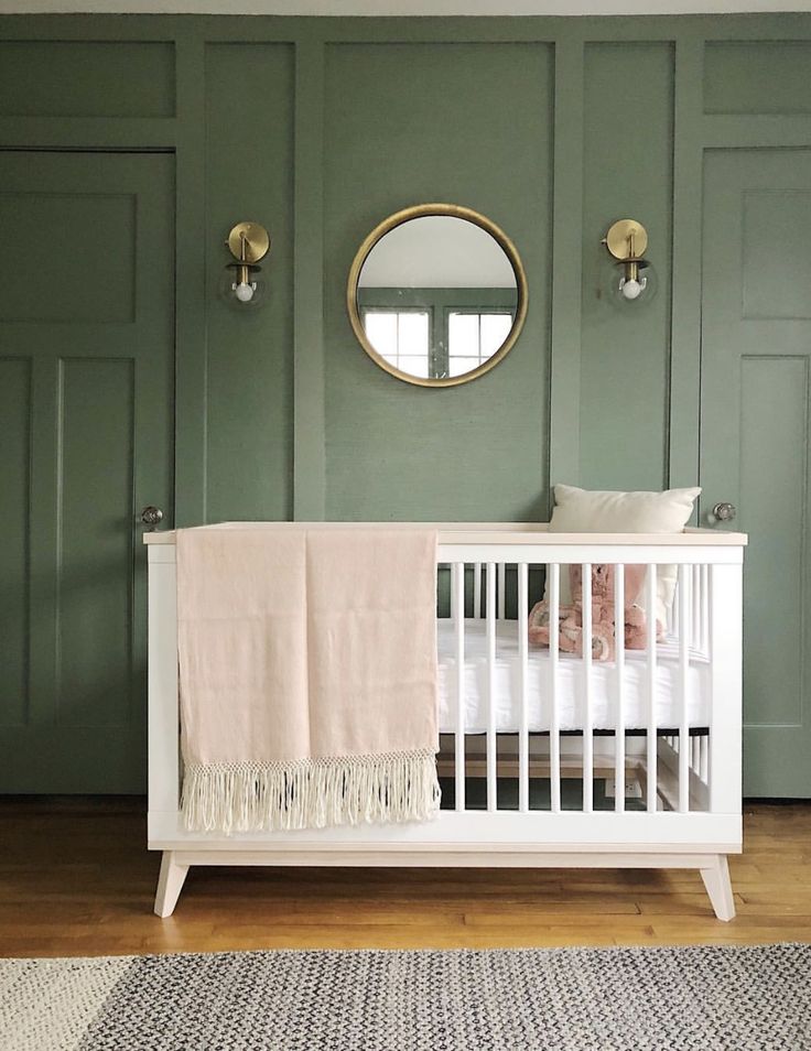 a white crib in front of green painted walls and a round mirror on the wall