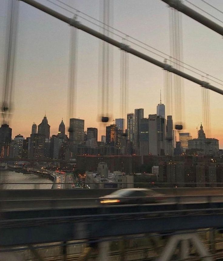 a view of the city skyline from a bridge at sunset or dawn with a car passing by