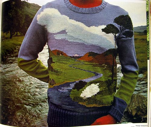 a man standing in front of a river wearing a sweater with trees and clouds on it