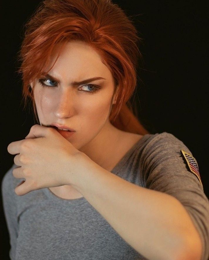 a woman with red hair and blue eyes is posing for a photo in front of a black background