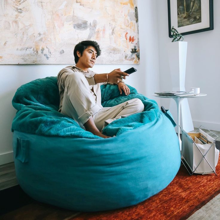 a man sitting on a bean bag chair with a remote control in his hand and looking at the camera