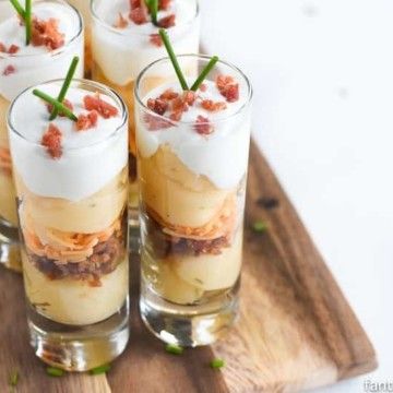 four glasses filled with dessert sitting on top of a wooden tray