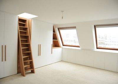 an empty room with two windows and a ladder in the corner, next to some bookshelves