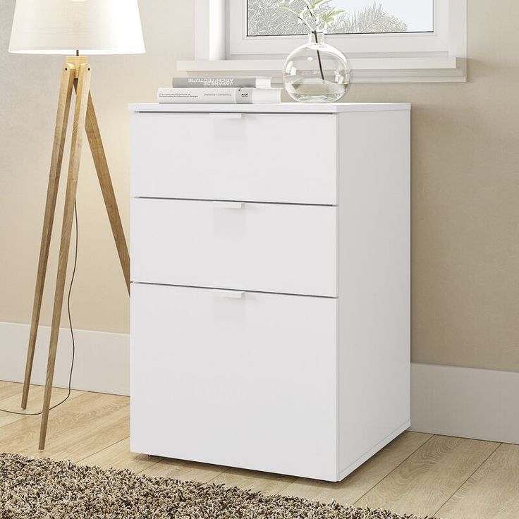 a white chest of drawers next to a lamp in a room with beige walls and carpet