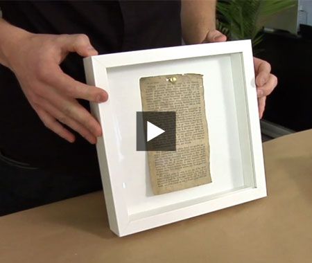 a person holding up a framed piece of paper with an old book page on it