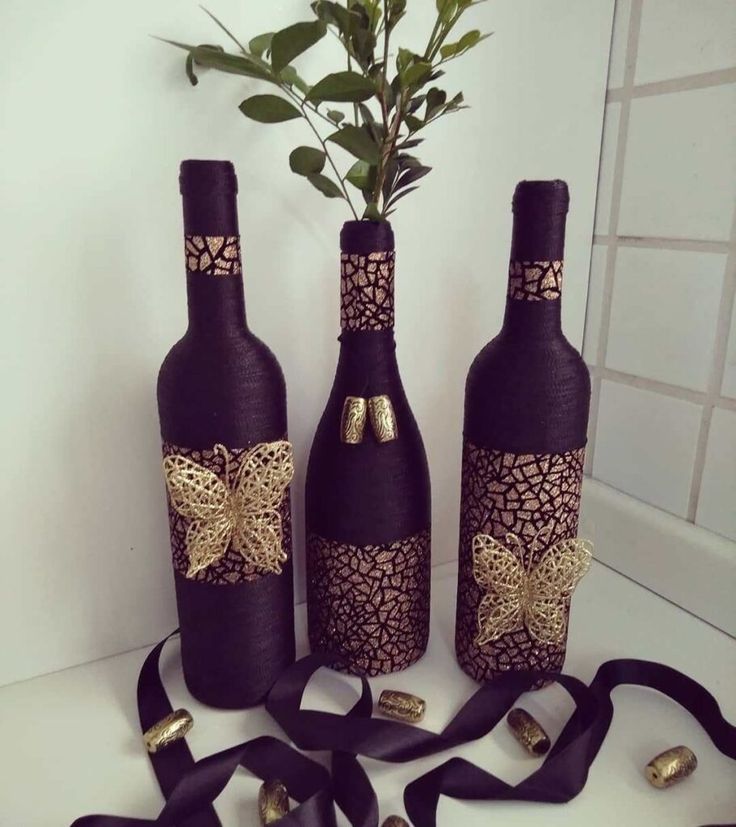 three wine bottles are decorated with gold and black ribbon, one has a flower in it