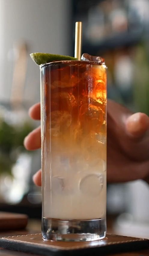 a person holding a glass with ice and a lime on the rim, in front of a bar