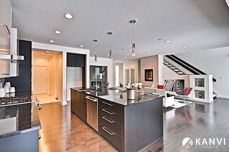 an open kitchen and living room area with hardwood floors, stainless steel appliances and white walls