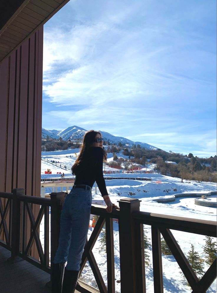 a woman standing on top of a balcony next to a snow covered field and mountains