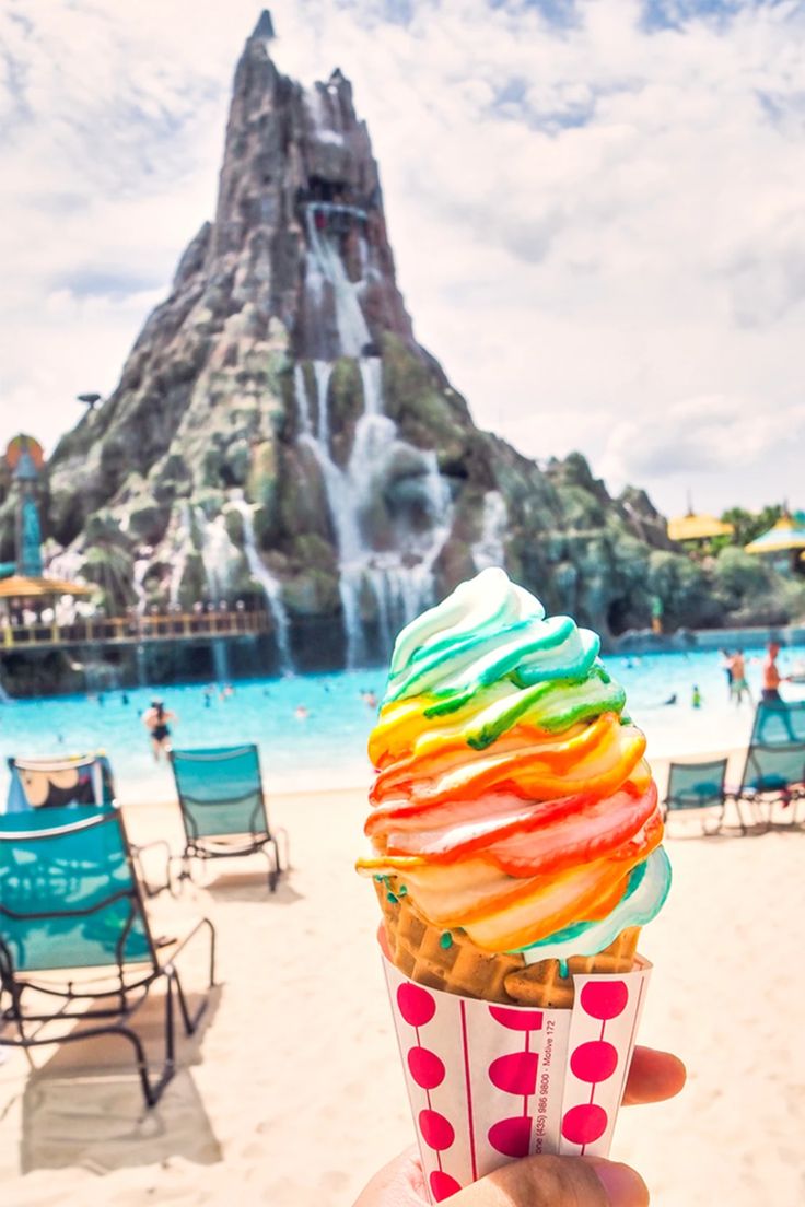 a person holding up an ice cream cone in front of a waterfall and beach area