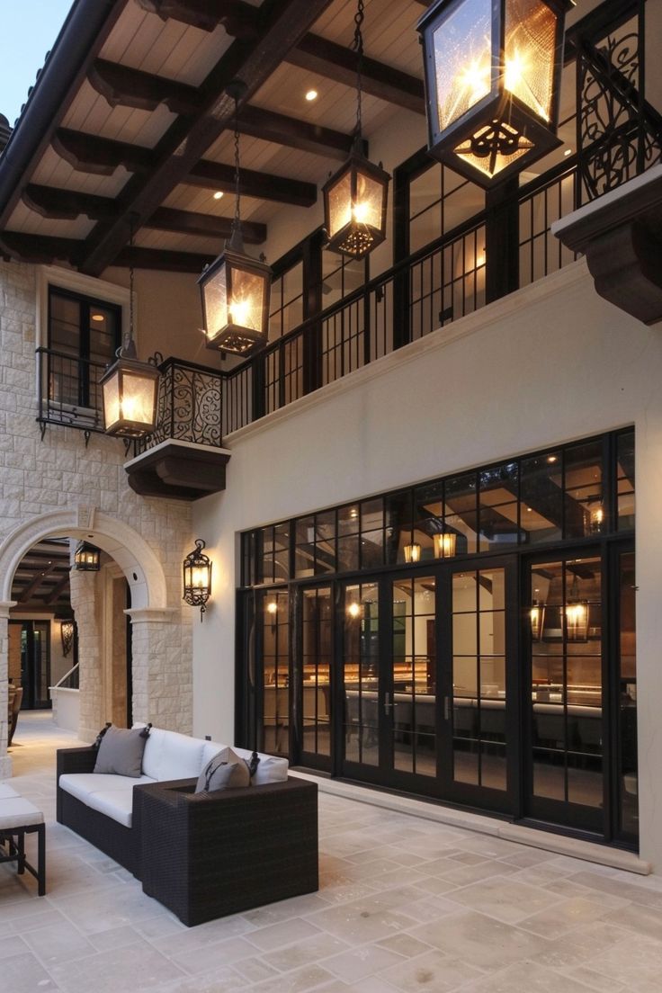 an outdoor living area with couches and lamps on the outside of the house at dusk