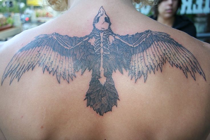 the back of a woman's neck with a large bird tattoo on her shoulder