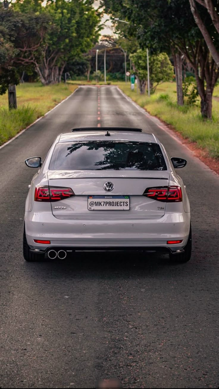 a silver car parked on the side of a road next to trees and grass in front of it