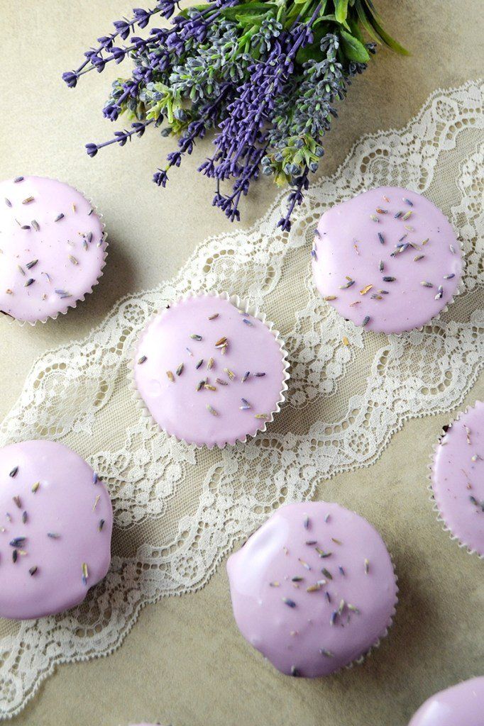 lavender cupcakes with sprinkles are on a lace doily next to flowers