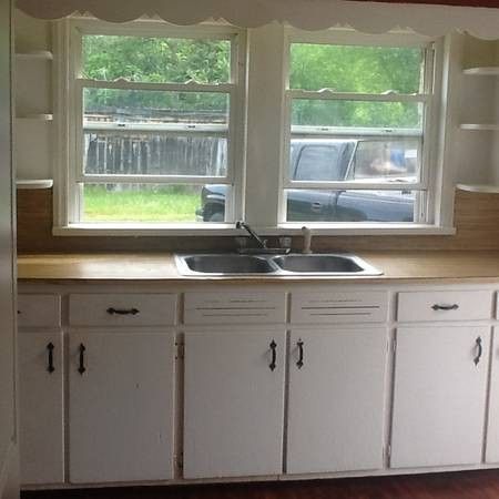 an empty kitchen with white cabinets and wood flooring is pictured in this image, there are two windows above the sink