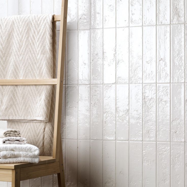 towels are stacked on a wooden chair in front of a white tiled wall