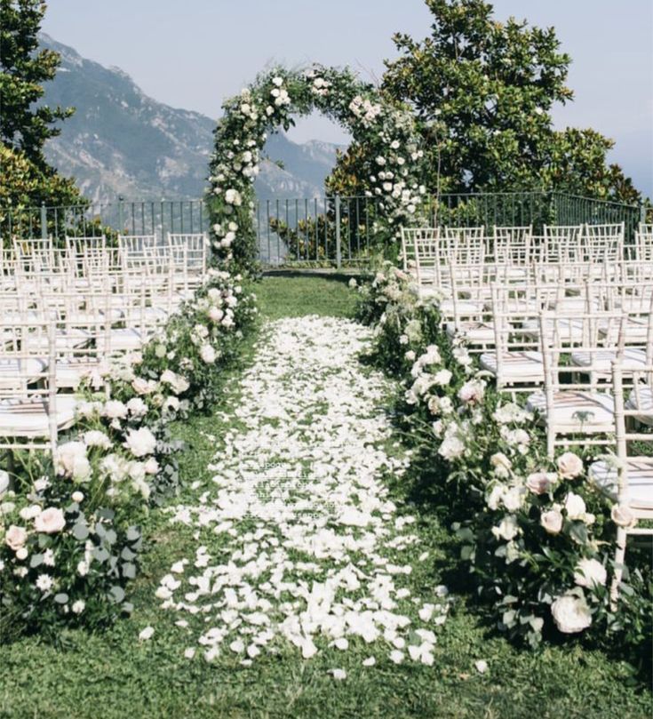 an outdoor ceremony set up with white flowers and greenery on the aisle, surrounded by chairs