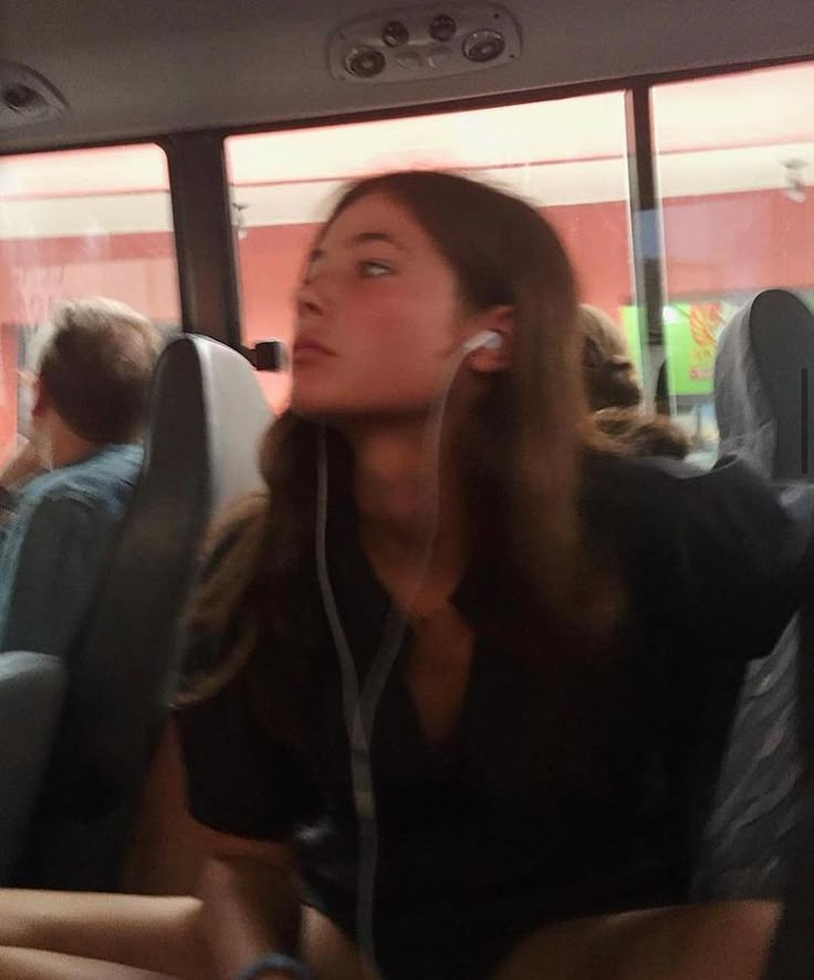 a woman sitting in the back seat of a bus listening to music on her headphones