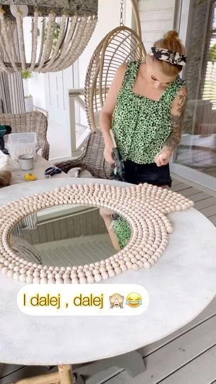 a woman standing in front of a table that has beads on it and an oval mirror