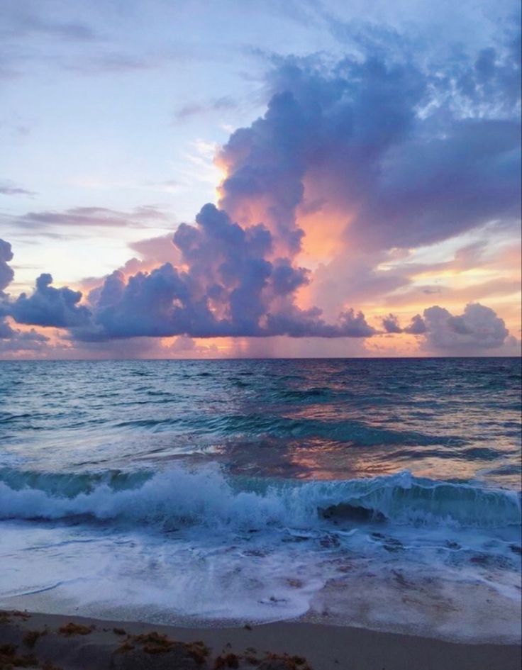 the sun is setting over the ocean with clouds in the sky and waves on the beach