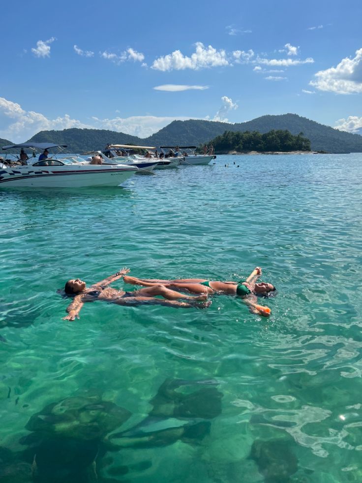 two people floating in the water near boats