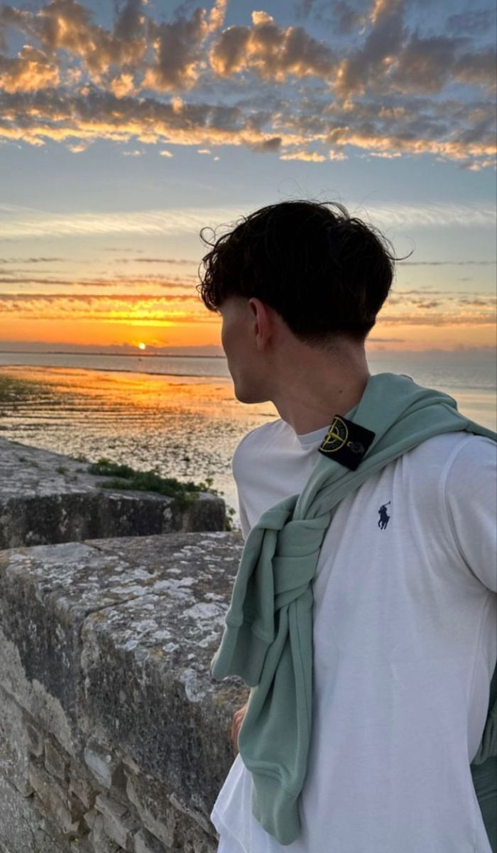 a man standing on top of a stone wall next to the ocean at sunset or dawn