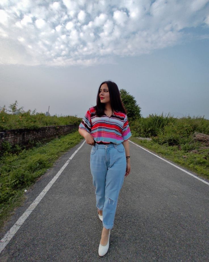 a woman walking down the middle of an empty road with her hands in her pockets