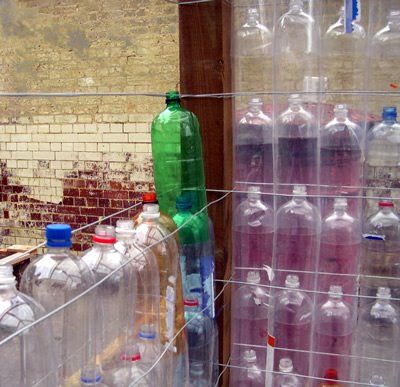 several plastic bottles are lined up on a wire fence near a brick wall and door