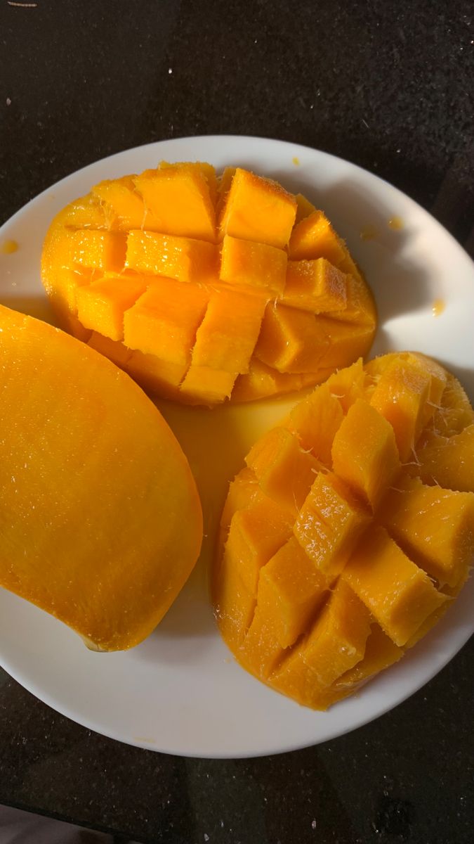 a white plate topped with cut up mangoes on top of a black countertop