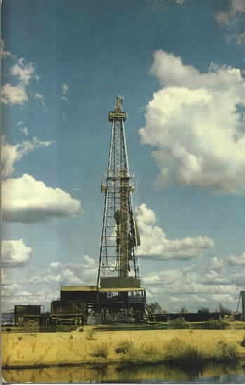 an oil rig sitting on top of a field next to a body of water with clouds in the sky