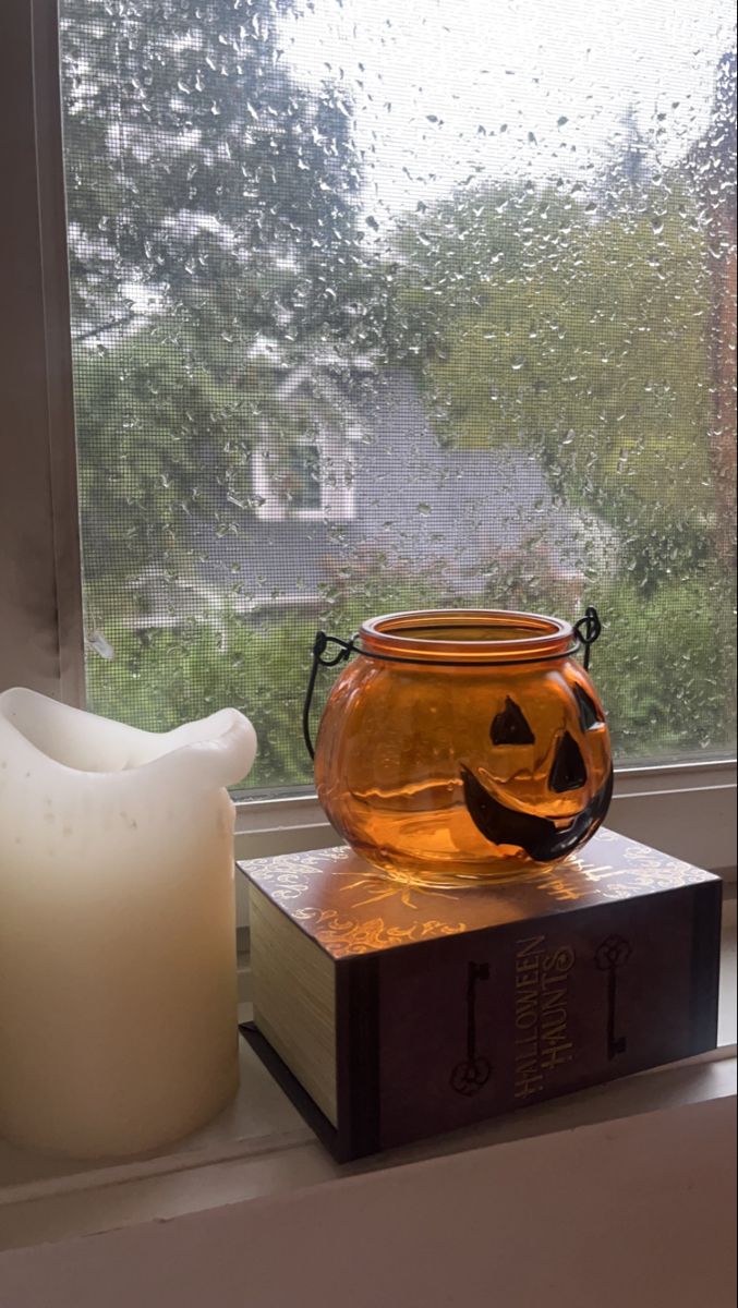 a candle sitting on top of a window sill next to a glass vase with a pumpkin face