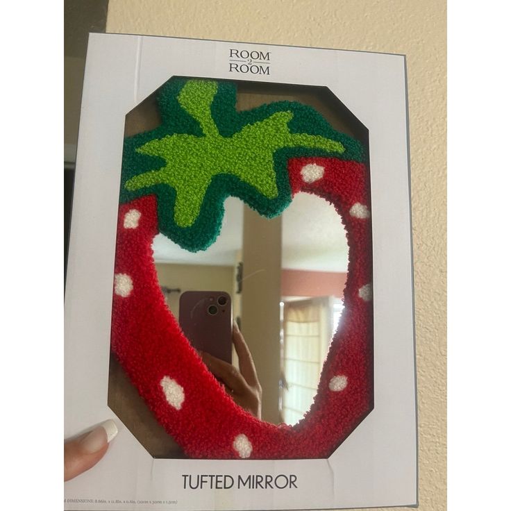 a hand holding up a mirror with a fake strawberry in the middle and green leaves on it