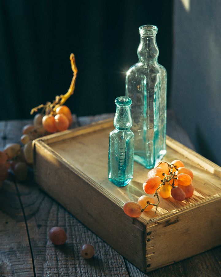 three glass bottles sitting on top of a wooden tray next to grapes and oranges