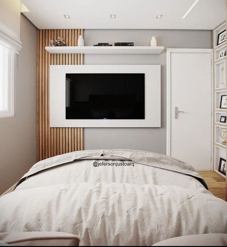 there is a television on the wall above the bed in this small room with white furniture