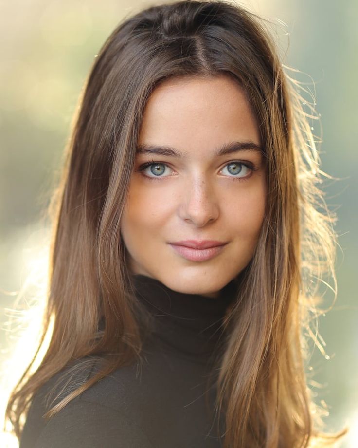 a woman with long hair and blue eyes posing for a photo in front of a blurry background