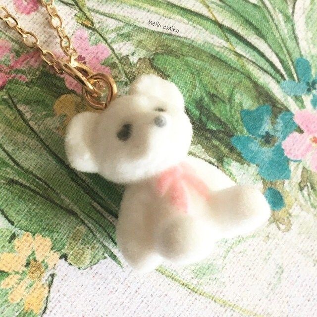 a small white teddy bear on a gold chain